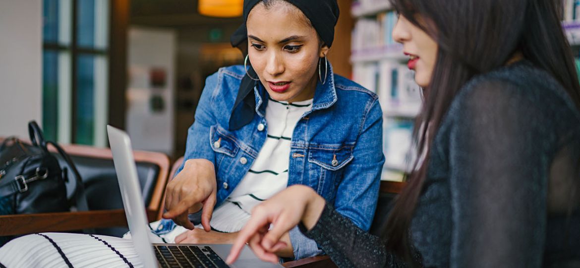 two-women-looking-and-pointing-at-macbook-laptop-1569076