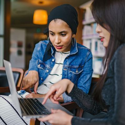 two-women-looking-and-pointing-at-macbook-laptop-1569076